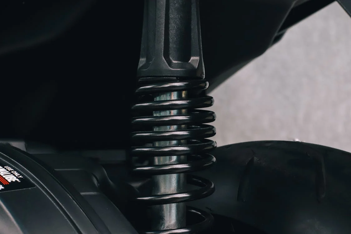 Close-up view of a car suspension coil spring and shock absorber, highlighting the metallic components and dark surrounding parts.